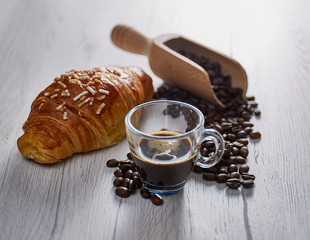 A croassant situated in the left and a cup of coffee on center