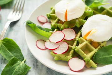 Healthy breakfast: spinach waffles with radish slices and poached eggs on green wooden table. Selective focus