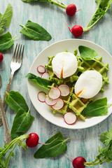 Healthy breakfast: spinach waffles with radish slices and poached eggs on green wooden table. Selective focus