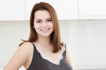 Serious attitude. Young smiling lady standing in a kitchen.