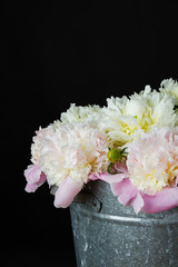 the bunch of peonies in a metal bucket on black