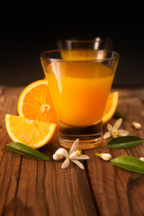 Orange juice in cup of glass with blossom, fresh fruits on wooden background
