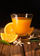 Orange juice in cup of glass with blossom, fresh fruits on wooden background