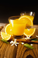 Fototapeta premium Orange juice in cup of glass with blossom, fresh fruits on wooden background