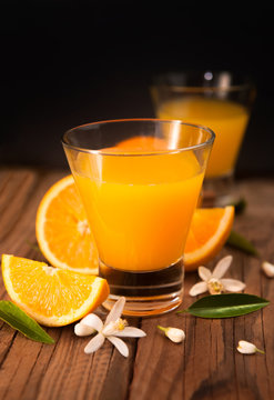 Orange juice in cup of glass with blossom, fresh fruits on wooden background