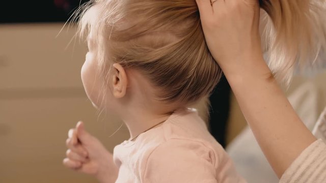 Mother makes daughter hairstyle indoors. 4k shot