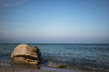 Fototapeta na wymiar Stones on coast of blue sea, blue sky. Rock and sea