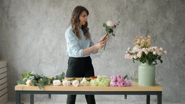 people, business, sale and floristry concept - happy smiling florist woman making bunch at flower shop, bouquet with peone and roses
