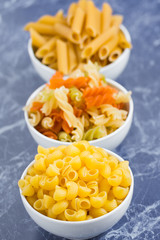 Variety of types of dry Italian pasta on blue marble table. Background