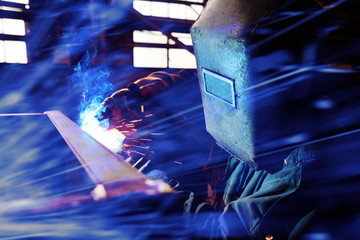 Welder in the helmet makes electronic welding for metal in the background of the plant