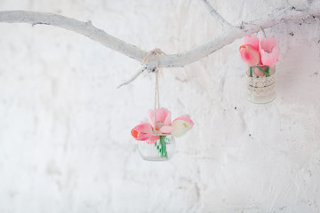 Tulips in vases hang on a decorative branch on a wall with white bricks