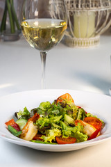 Vegetable salad with tomatoes and shrimps on the table in a composition with a glass of wine
