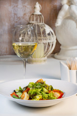 Vegetable salad with tomatoes and shrimps on the table in a composition with a glass of wine