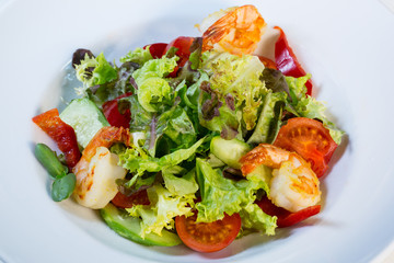 Vegetable salad with tomatoes and shrimps on the table in a composition with a glass of wine
