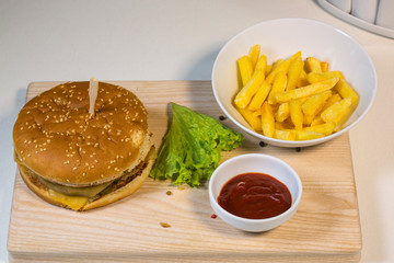 Burger with potatoes on a wooden board in a composition on a table