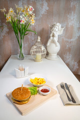 Burger with potatoes on a wooden board in a composition on a table