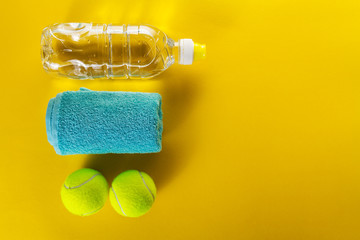 Healthy Life Sport Concept. Tennis Balls, Towel and Bottle of Water on Bright Yellow Background. Copy Space. Flat Lay.