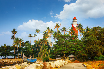 Thangassery Lighthouse on the cliff surrounded by palm trees and big sea waves on the Kollam beach. Kerala, India