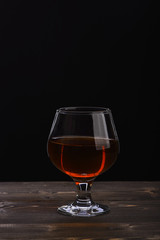 glass with cognac or whiskey on black wooden table