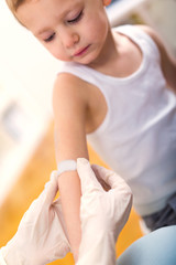 Doctor in her practice putting a bandage on some hurt of a little boy child