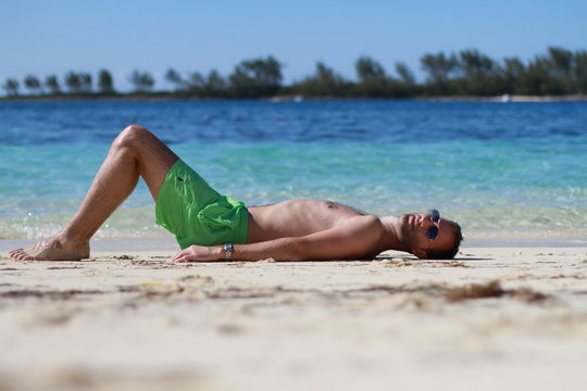 Homme au maillot vert fluo bronsant sur la plage de Nassau, Bahamas