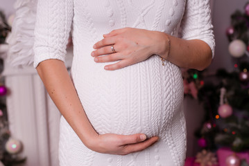 Pregnant girl in a white dress hugging her stomach.