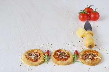 White rustic background with homemade biscuit in a form of pizza with chili,rosemary, cherry tomatoes, parmezan, cheese knife and spices. Space for text