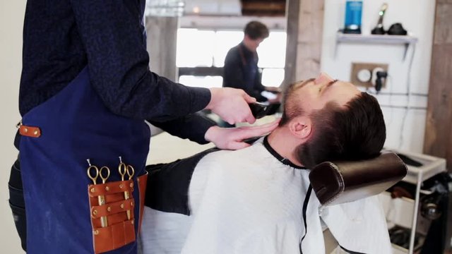 man and barber with trimmer trimming beard at shop