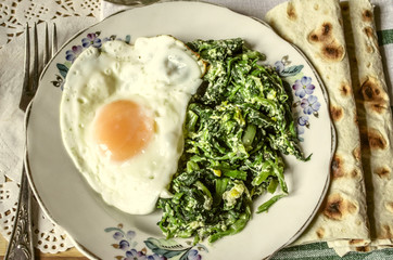 
 Spinach with fried eggs and pita on striped chopping board with napkin and fork
