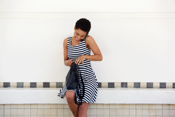 Young african woman talking on mobile phone and looking in bag