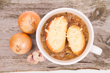 Onion soup with toast on a wooden background with some onions and garli