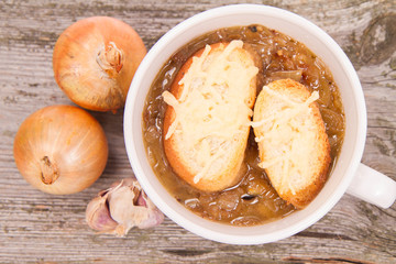 Onion soup with toast on a wooden background with some onions and garlic