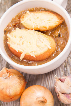 Onion soup with toast on a wooden background with some onions and garlic