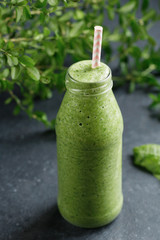 Close-up of a glass bottle with green spinach detox smoothies on black background. Healthy eating.
