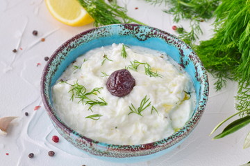 Homemade Greek traditional sauce tzatziki with cucumber, garlic, yogurt , olive oil and lemon in a traditional colored bowl on a white background. Healthy eating concept. Mediterranean lifestyle