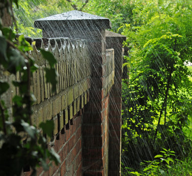Alte Backsteinmauer um einen Garten, über die Wasser aus einem Gartenschlauch spritzt