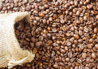Coffee beans in coffee bag made from burlap on wooden surface. Focused in middle of the frame.