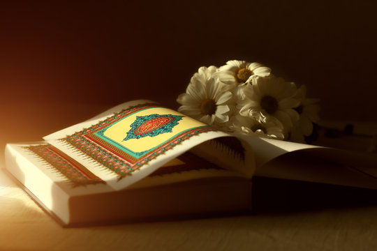 Quran - The Holy Book Of Islam Open  With Flowers In  Sunrays