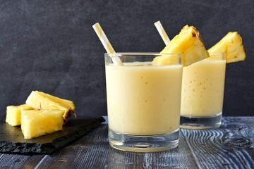 Two glasses of tropical pineapple smoothie against a dark background