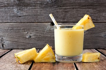 Healthy pineapple smoothie in a glass with scattered fruit against a rustic wood background