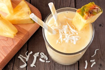 Tropical pineapple coconut smoothie above scene against an old wood background