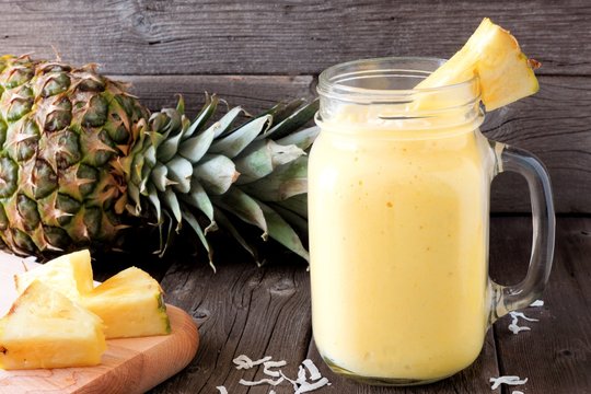 Pineapple smoothie in a mason jar, scene against an old wood background
