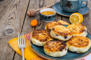 Hot cheesecake with raisins and honey on plate on wooden backgro