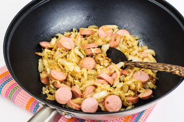 Stewed cabbage with sausages in frying pan over white background