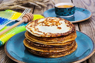 Hot pancakes with honey in vintage bowl on background of an old 