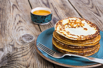 Hot pancakes with honey in vintage bowl on background of an old 