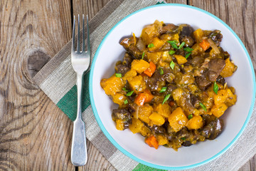 Vegetable stew with pumpkin and mushrooms on wooden background. 
