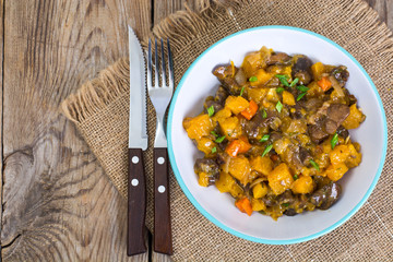 Vegetable stew with pumpkin and mushrooms on wooden background. 