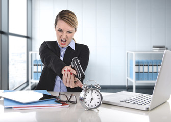 business woman furious and angry working with computer laptop pointing gun to alarm clock