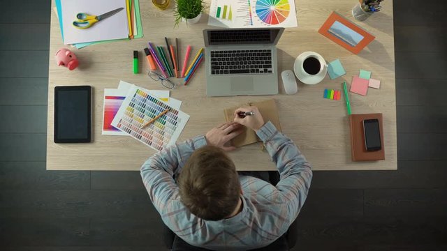 Male designer making notes in his notebook to discuss them with client, top view